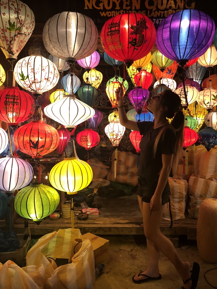 Woman surrounded by colorful lanterns in a market.