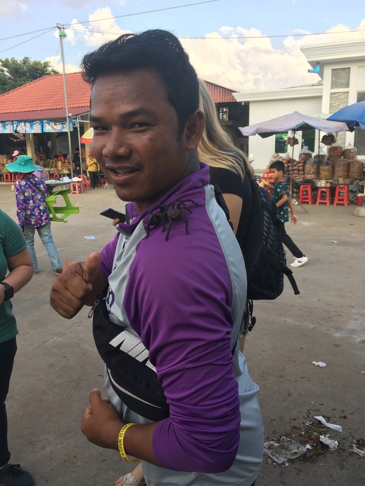 Homme tenant une grosse araignée sur son épaule en faisant un pouce levé.