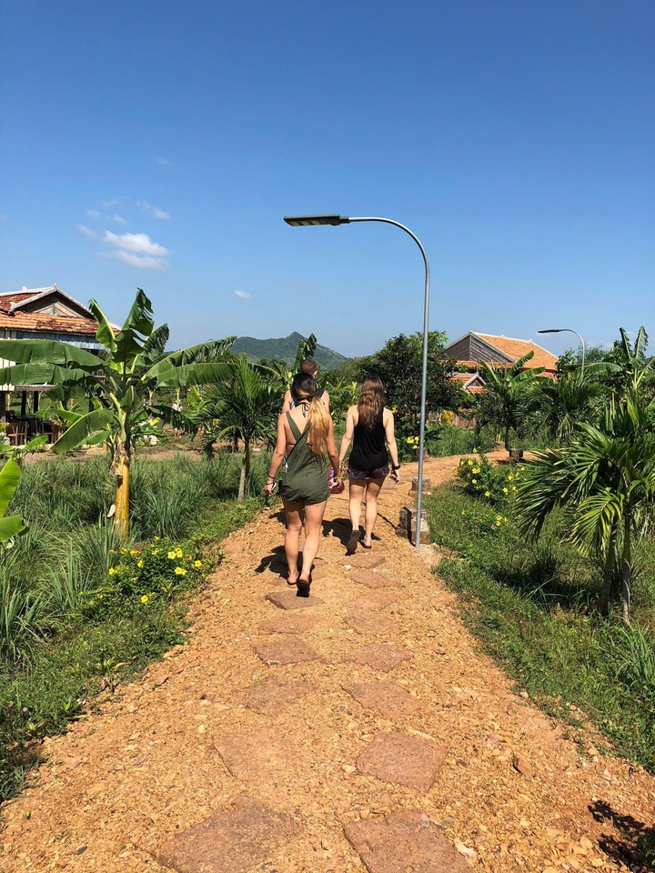 Three women walking along a garden path with tropical plants.