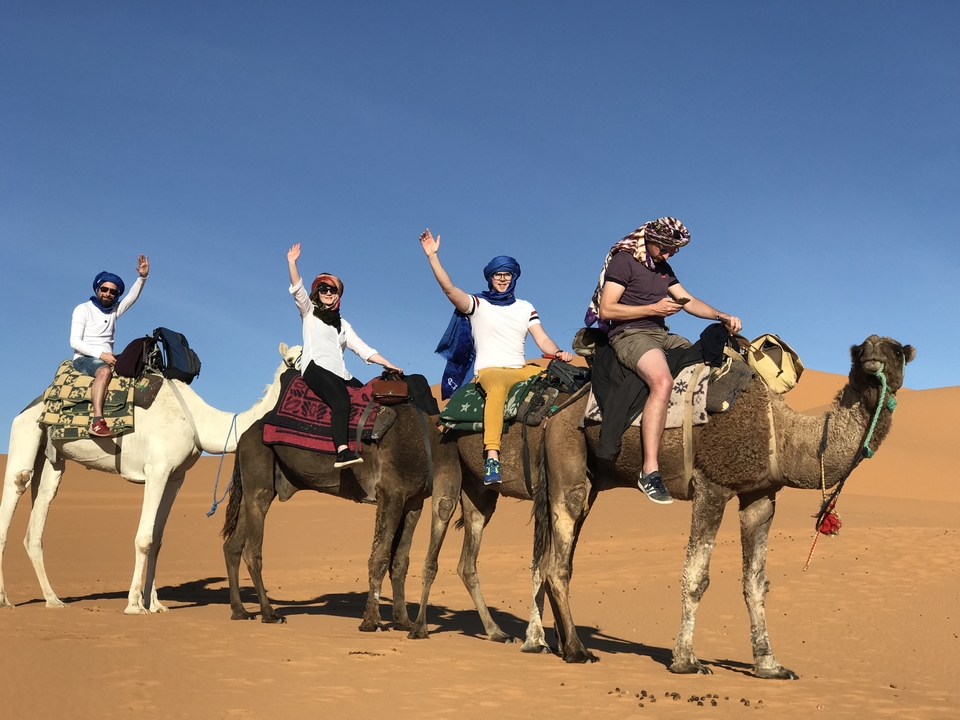 Group riding camels in the desert with blue sky.