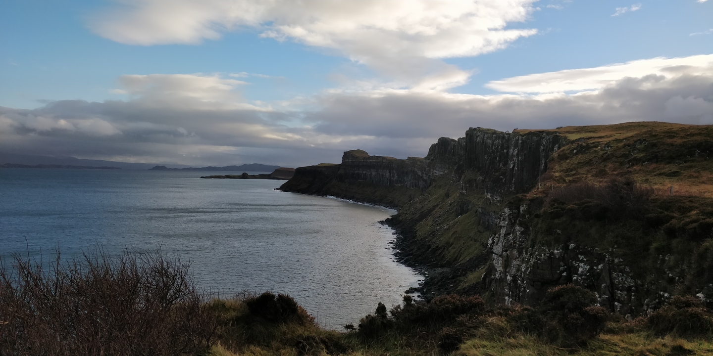 A dramatic coastline with cliffs and a cloudy sky.