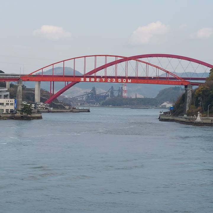 Red bridge over a body of water with mountains in the background.