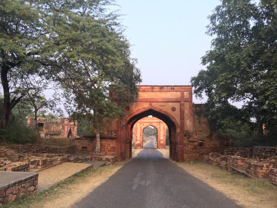 A red sandstone gate with trees lining the road.