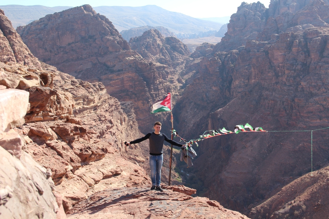 Person standing on a cliff with a flag overlooking canyon landscape.