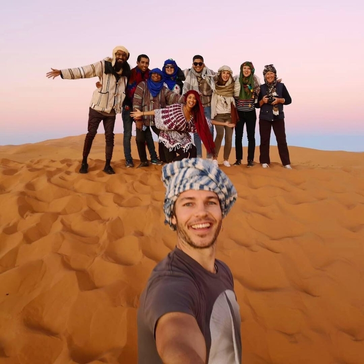 A group of people posing on sand dunes with vibrant sky.