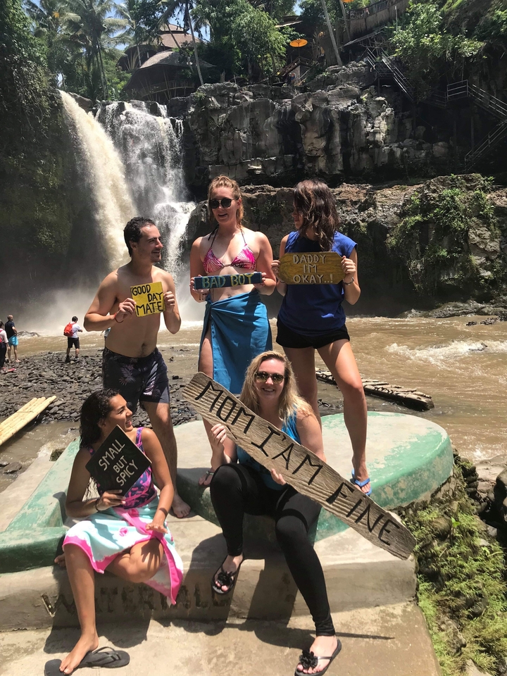 Group holding different signs in front of a waterfall.