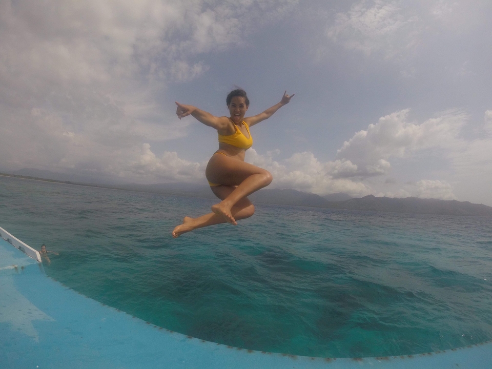 Person jumping into the water from a boat with mountains in the background.