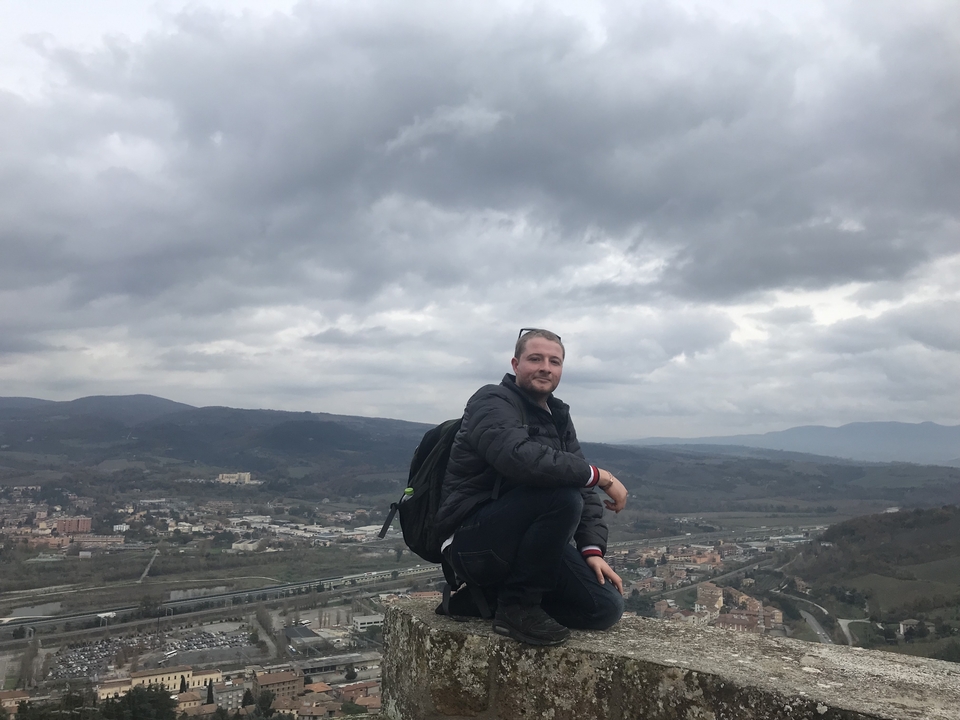 Person sitting on a viewpoint with a landscape in the background.