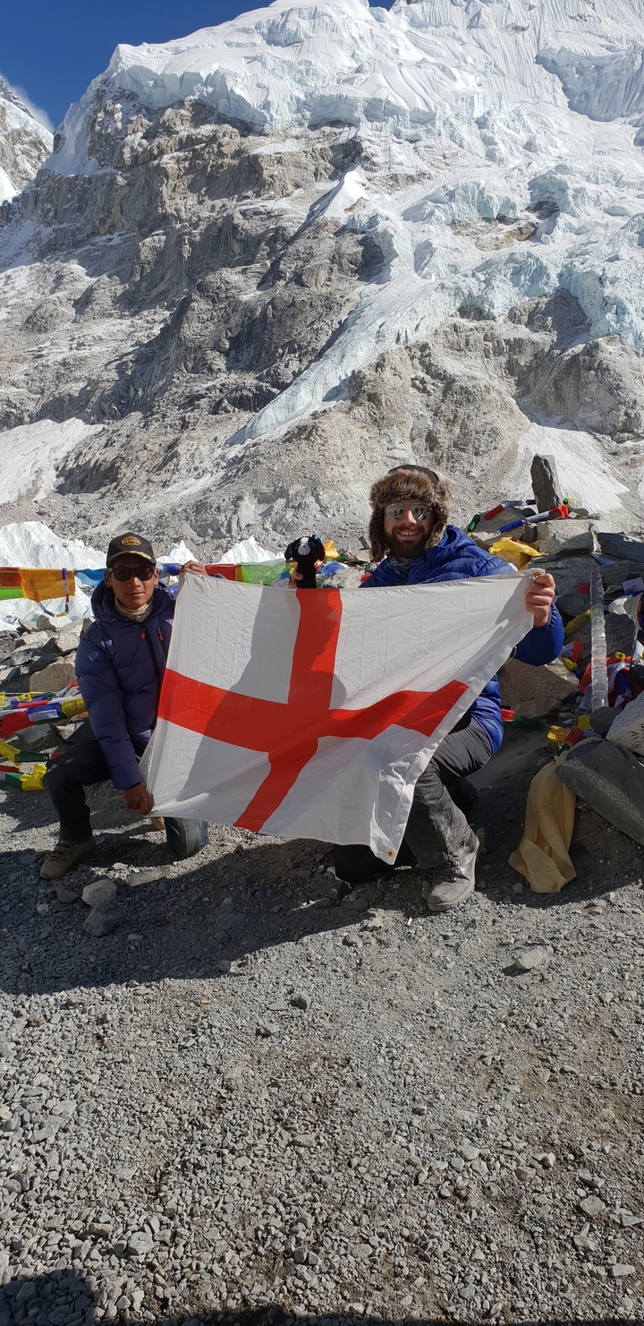 Two people holding a flag in front of prayer flags.
