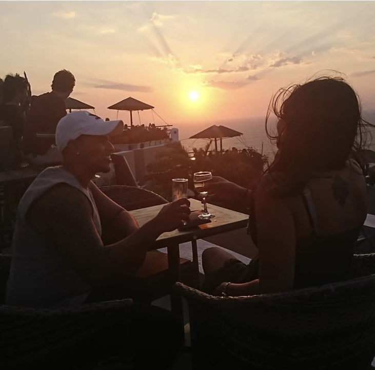 Two people clinking glasses at a table during sunset.