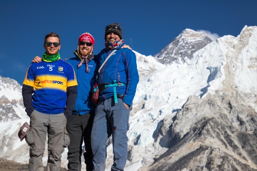 Three people posing with snowy mountains in the background.