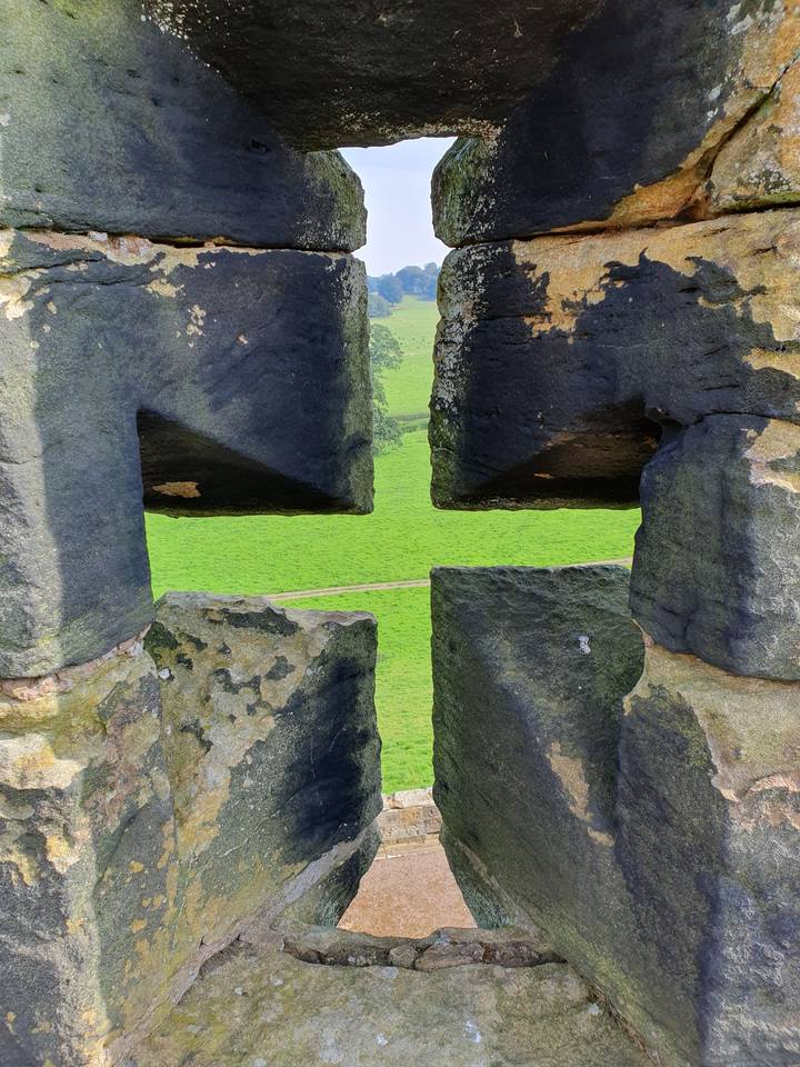 View through a historic castle opening overlooking green fields.