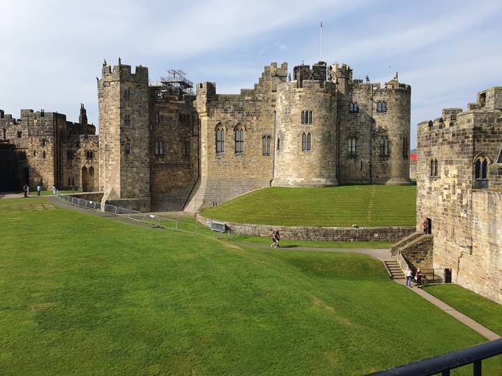 Large stone castle with grassy courtyard and tourists.