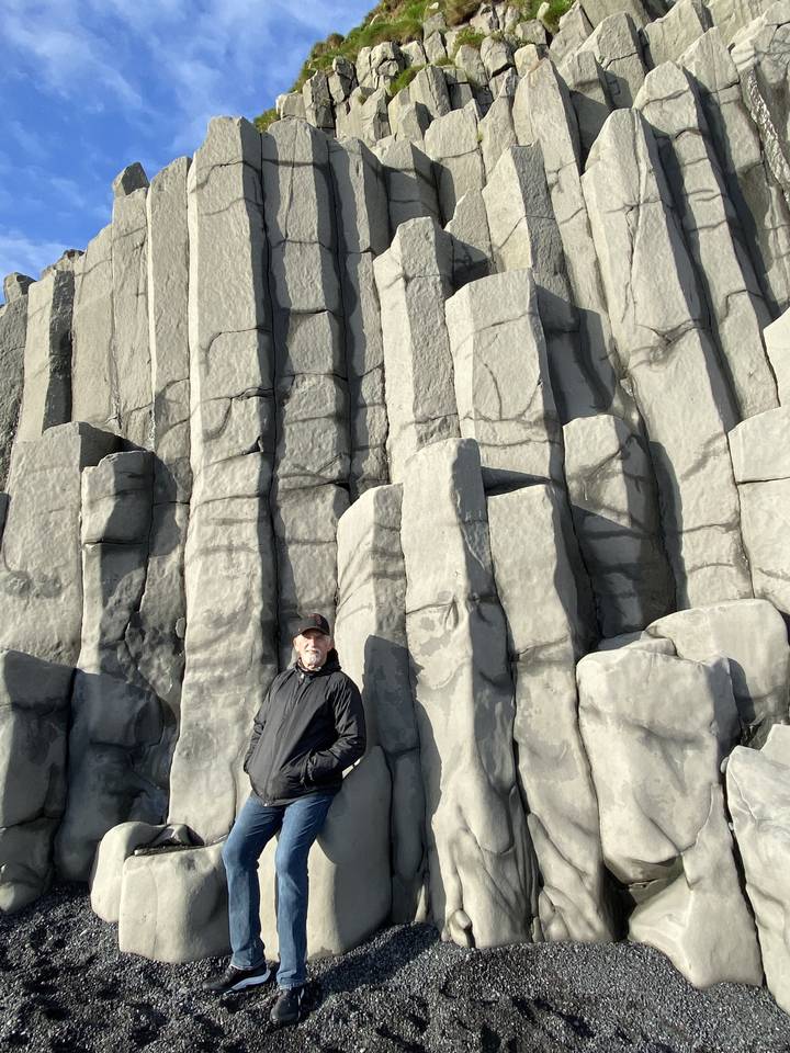 Person posing against basalt columns on a black sand beach.