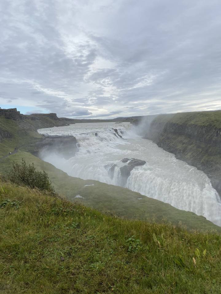 Waterfall flowing over cliffs, visible through grassy hills.