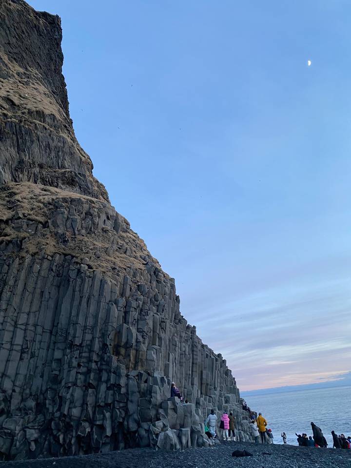 Basalt columns along a beach with people observing the formation.