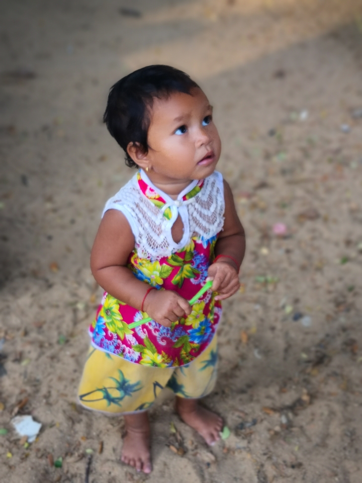 A young child in vibrant clothes standing on sand.