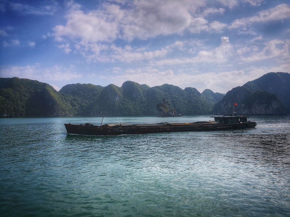 Boat sailing on a calm sea with green mountains in the background.