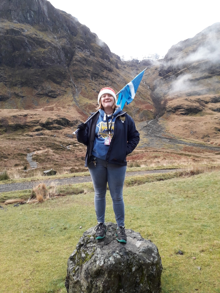 Person holding a flag in a grassy area with hills in the background.