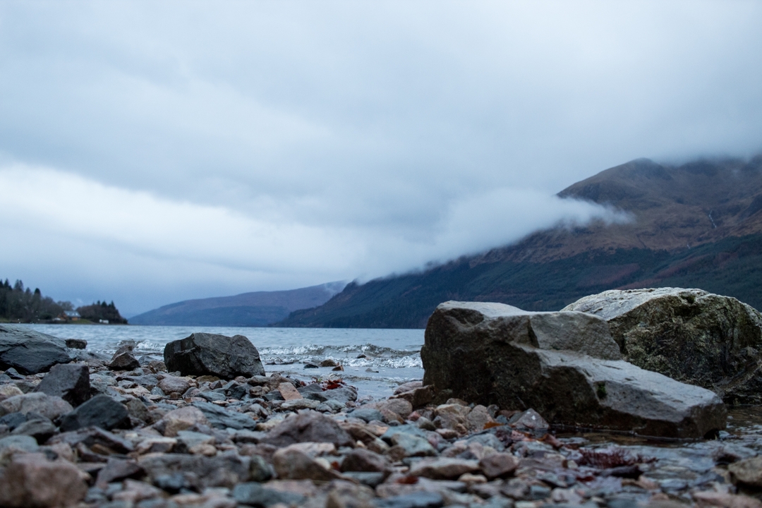 Rocks by a lake with misty mountains in the background.