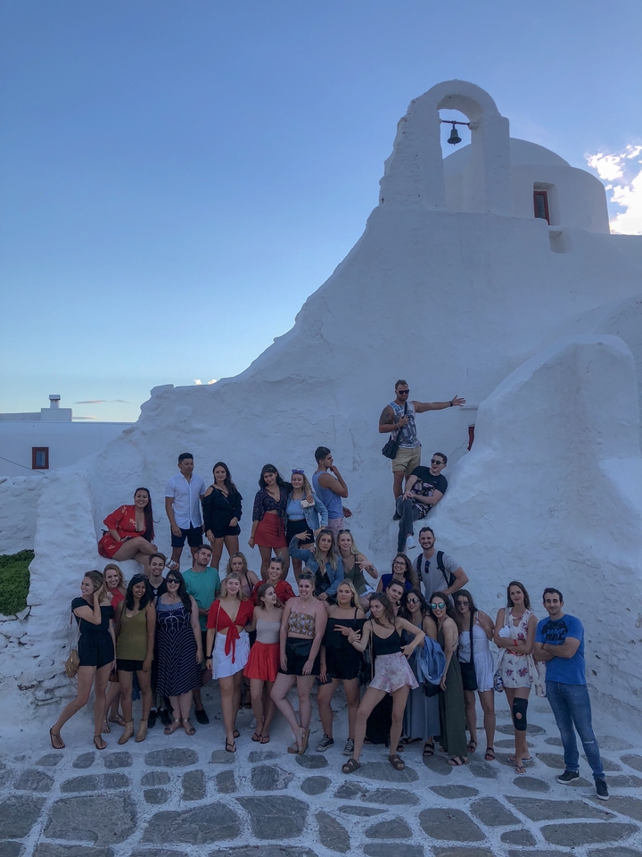 Group of people posing in front of a white stucco building.