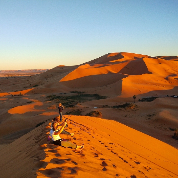Two people sitting on a dune in a desert landscape.