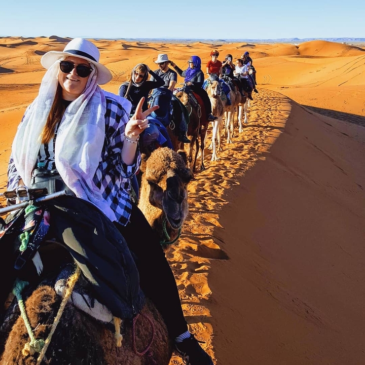 Camel caravan with people riding through a desert.