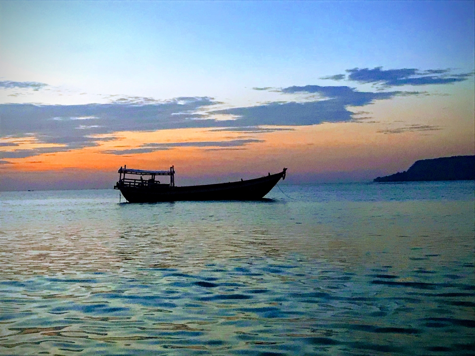 A boat on a calm sea during a colorful evening sky.