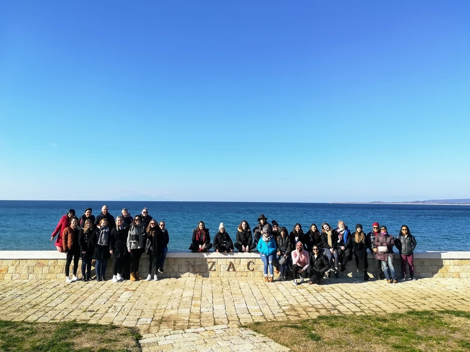 A large group of people posing by the sea with ANZAC engraved.
