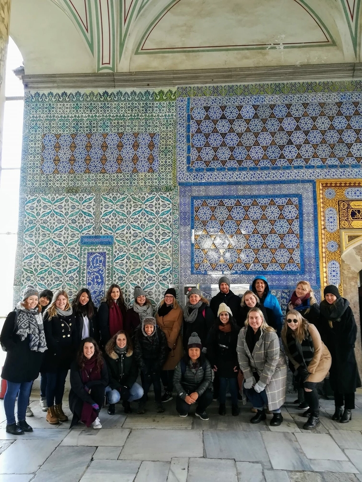 A group of people in front of a wall with patterned tiles.