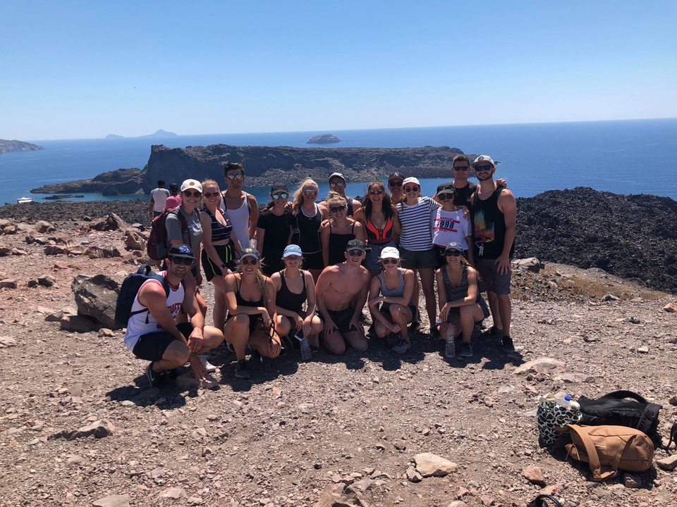Large group of people posing on a rocky landscape with ocean view.