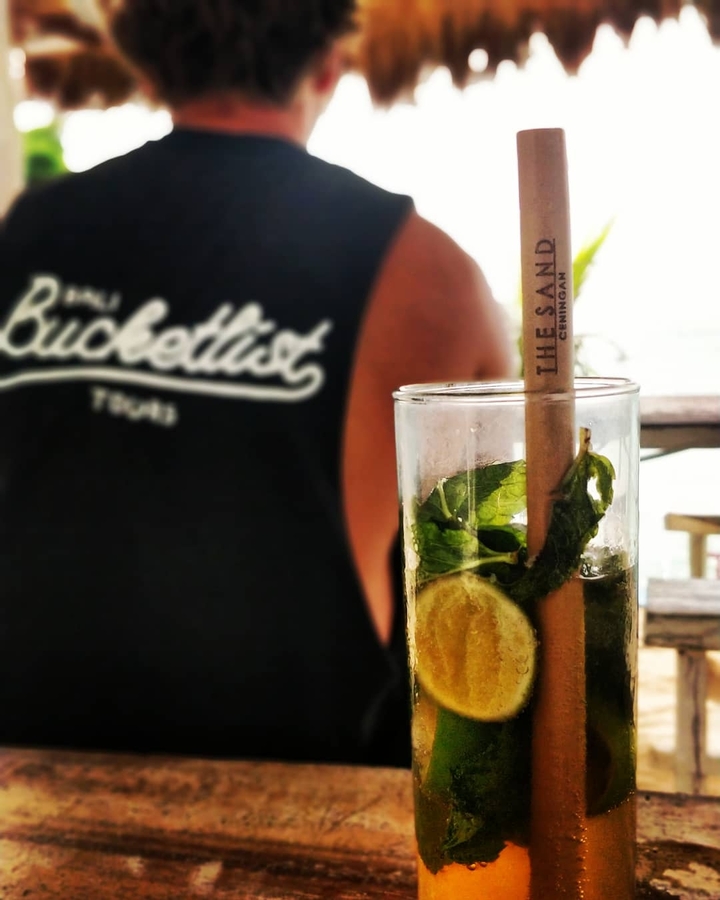 Close-up of a drink with mint leaves and a straw with a person wearing a shirt in the background.
