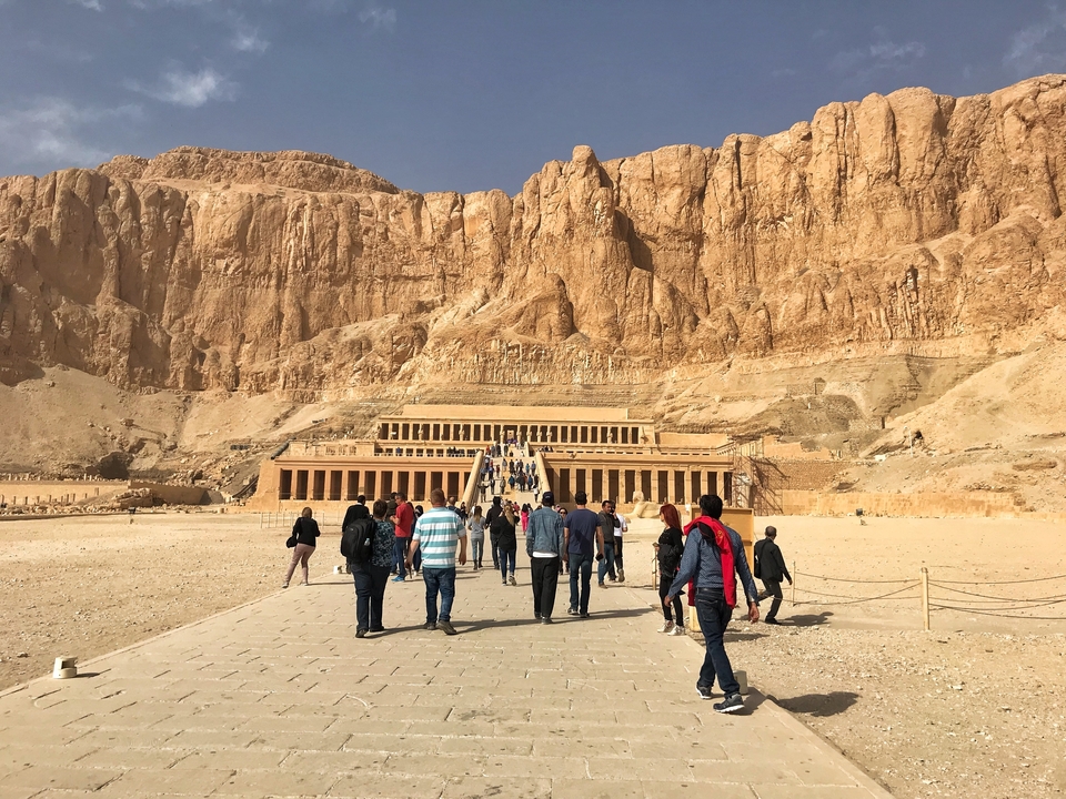 Tourists walking towards a large temple carved into a cliff.