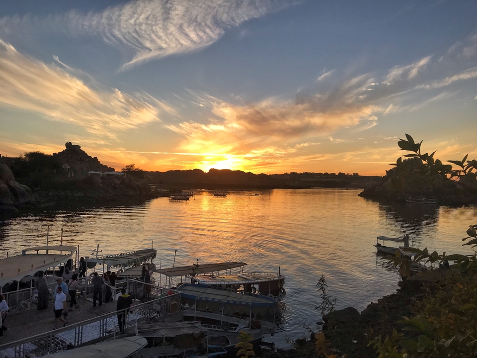 Sunset over a river with boats and distant hills.