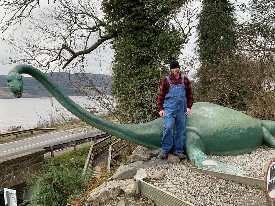 Person standing next to a large dinosaur sculpture.