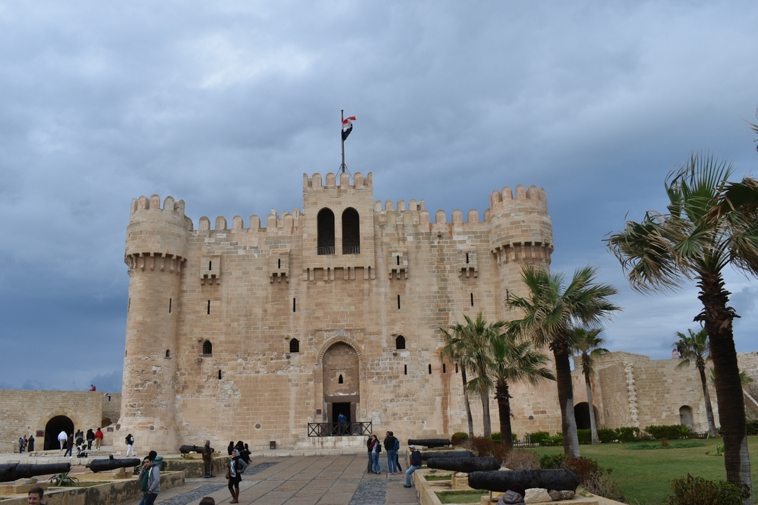 Historic fortress with palm trees, under a cloudy sky.