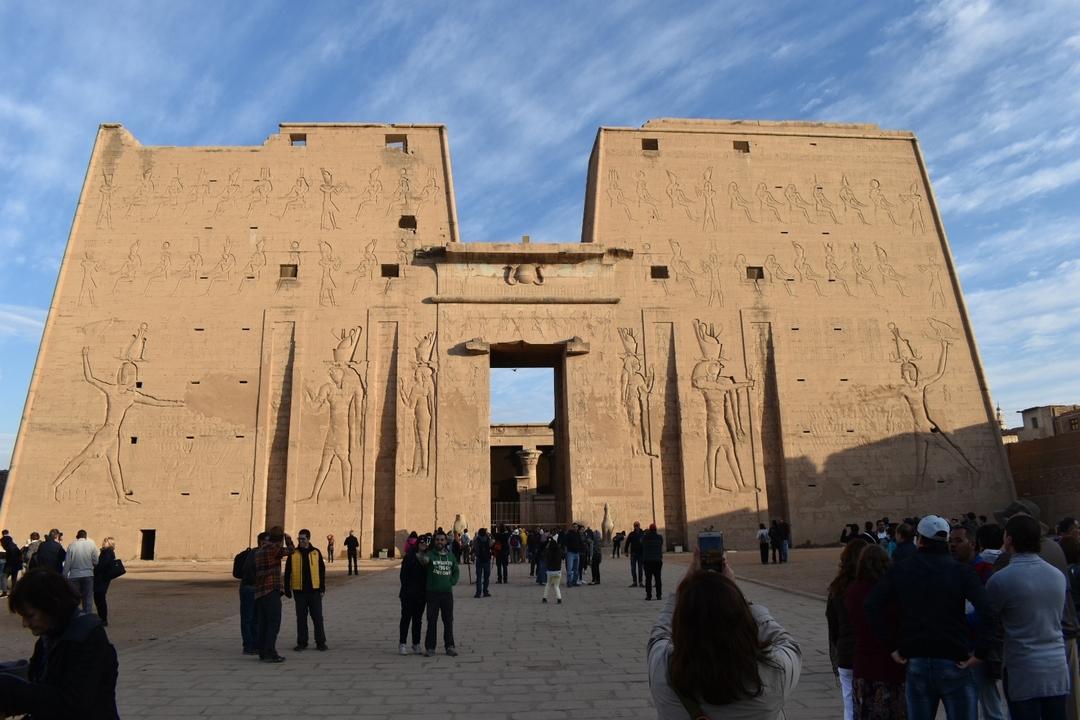 Facade of a large ancient Egyptian temple with people in front.