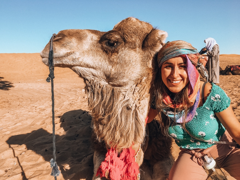 Smiling woman standing next to a camel in the desert.