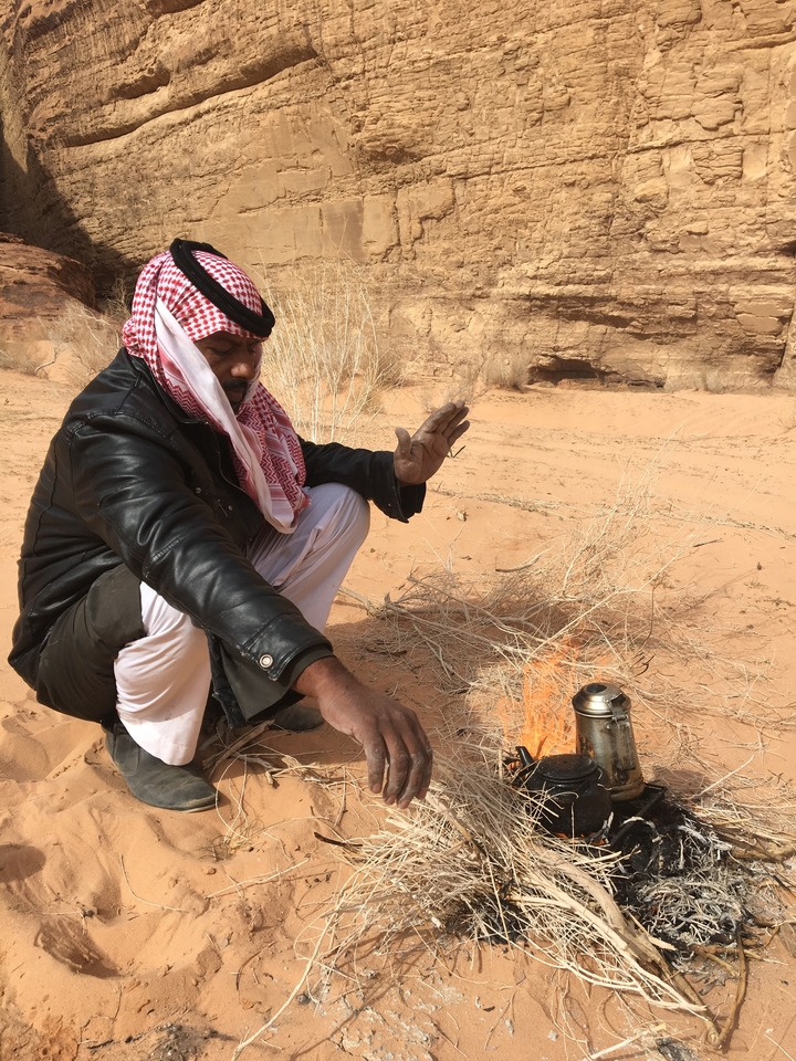 Homme assis près d'un feu de camp dans le désert avec une bouilloire.