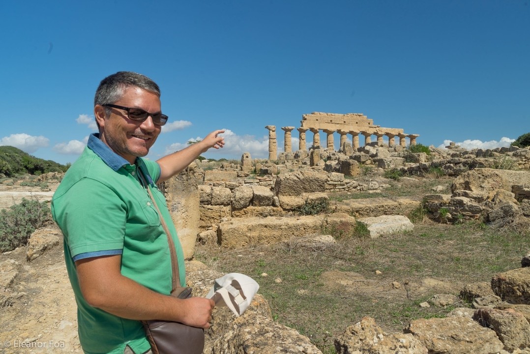 Homme souriant pointant du doigt des ruines de temple antique.