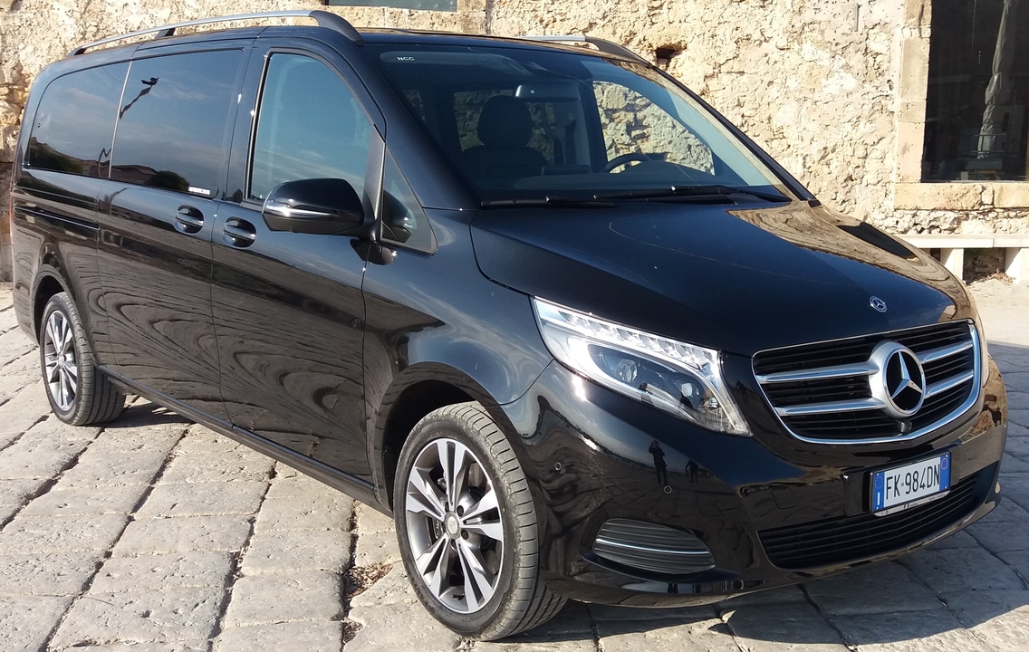 Un van Mercedes noir garé devant des bâtiments en pierre.