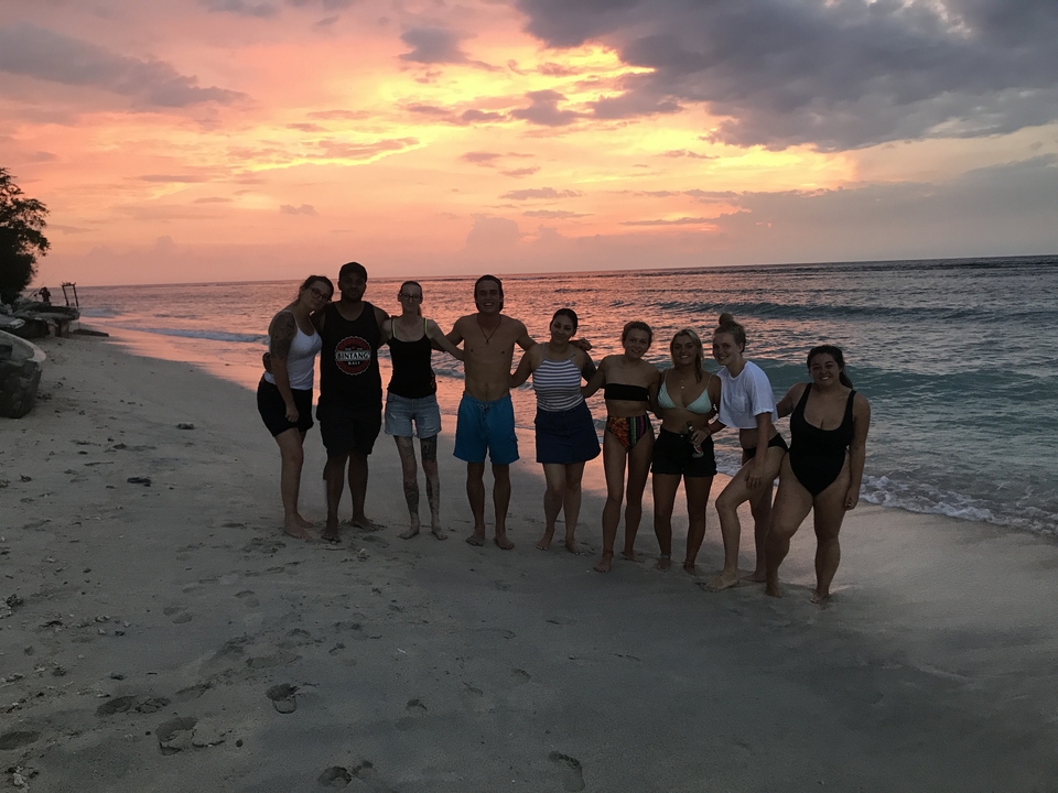 Group of people posing on a beach at sunset.