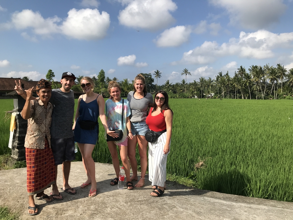A group poses in front of rice fields on a sunny day.