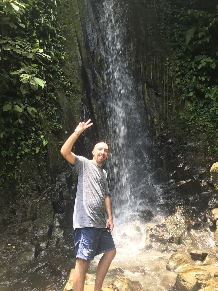 Person posing with a peace sign in front of a waterfall.