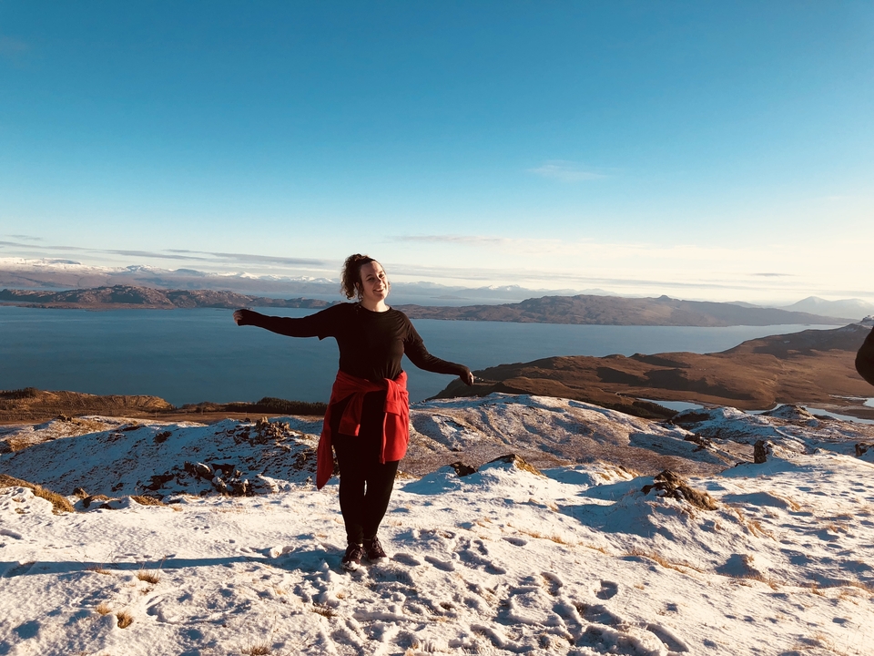 Person standing atop a snowy mountain with a vast view.