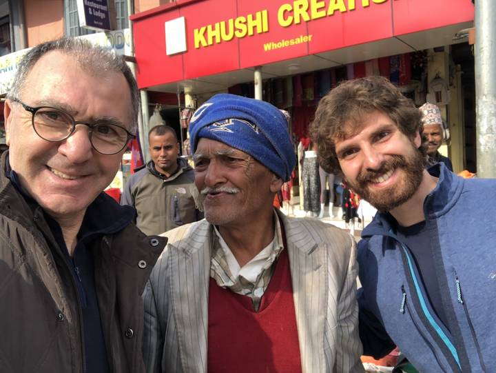 Deux hommes posant avec un vendeur local dans une rue.