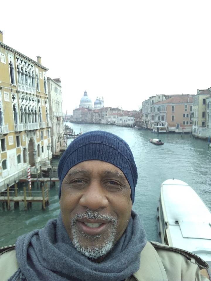 A man on a bridge over the Grand Canal with a view of Santa Maria della Salute in Venice.