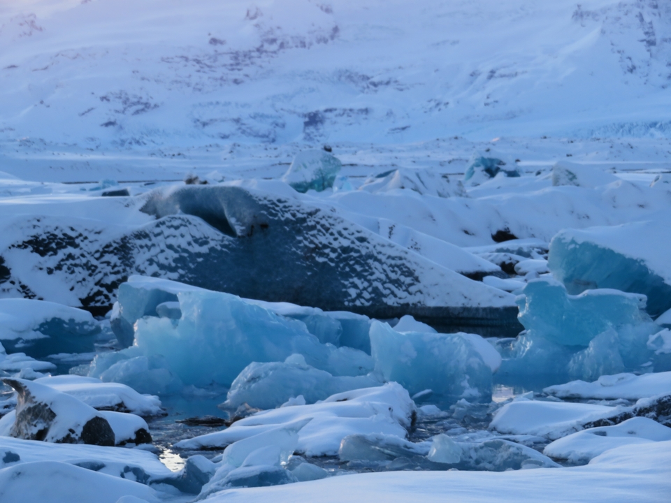 Icebergs floating in a body of water surrounded by snowy mountains.