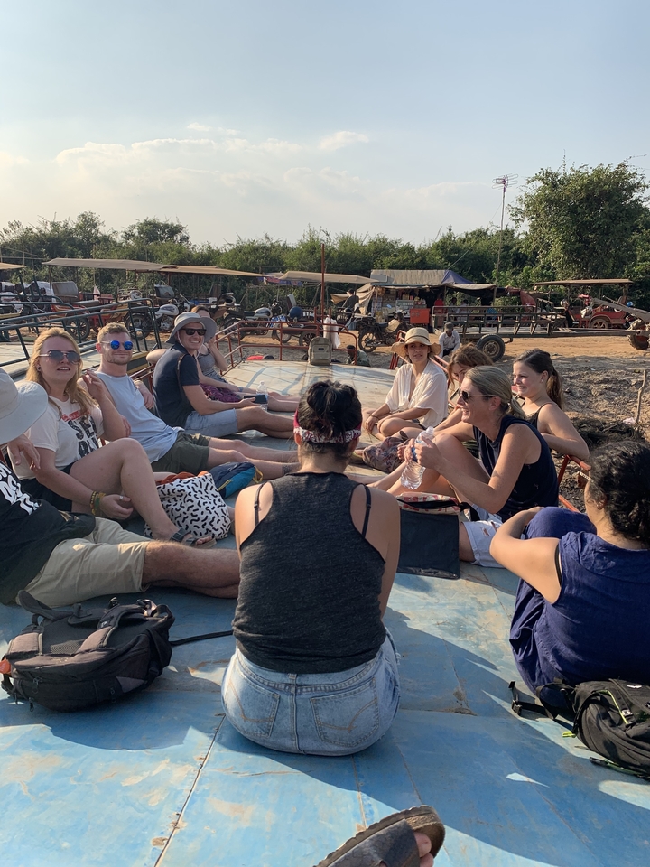 People sitting together outdoors, under a sunny sky with some machinery in the background.