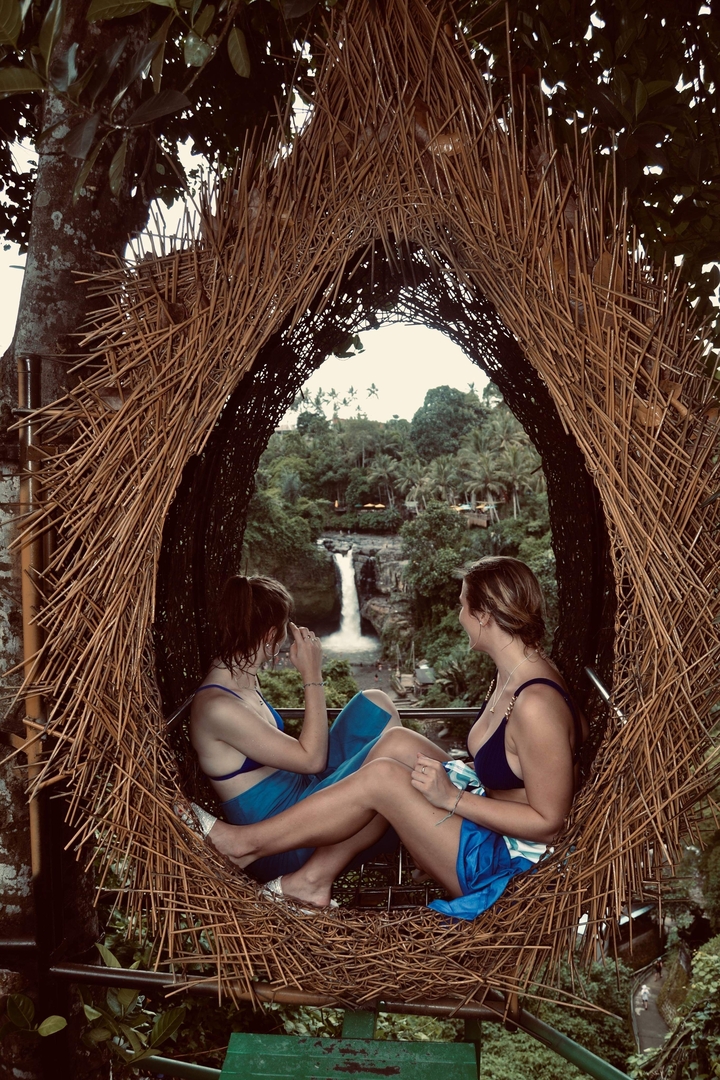 Two women enjoying a view of a waterfall framed by a bamboo structure.